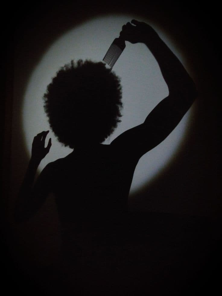 A figure lifting a pick through a full natural afro, caught in a pool of light